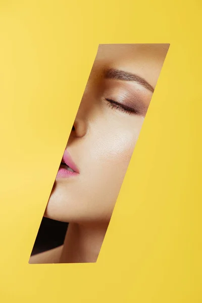 Female face with closed eyes in hole in yellow paper — Stock Photo