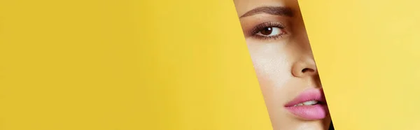 Woman looking at camera across quadrangular hole in yellow paper, panoramic shot — Stock Photo