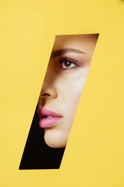 Female face with makeup in quadrangular hole in yellow paper on black — Stock Photo