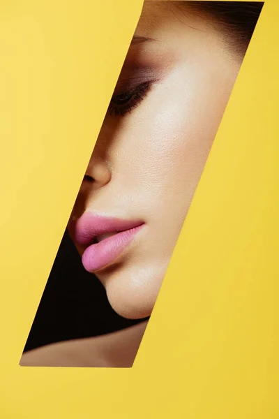 Female face with pink lips in quadrangular hole in yellow paper on black background — Stock Photo