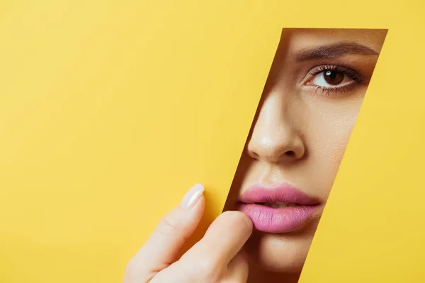 Mujer con labios rosados mirando a la cámara a través del agujero cuadrangular y tocando papel amarillo - foto de stock