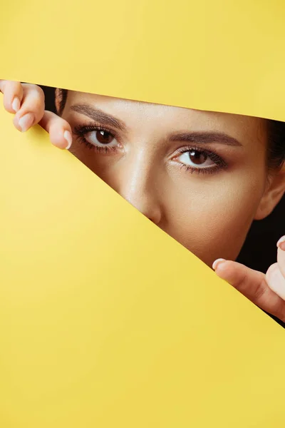 Женщина смотрит в камеру через отверстие и трогает пальцами желтую бумагу — стоковое фото
