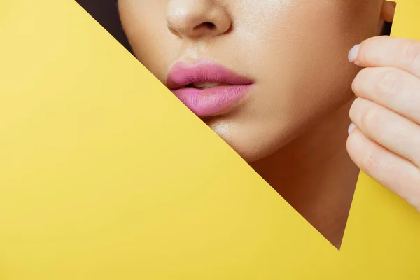 Cropped view of woman with pink lips in triangular hole touching yellow paper on black — Stock Photo