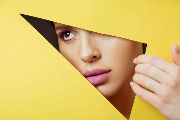 Woman with pink lips in triangular hole touching yellow paper with hand — Stock Photo