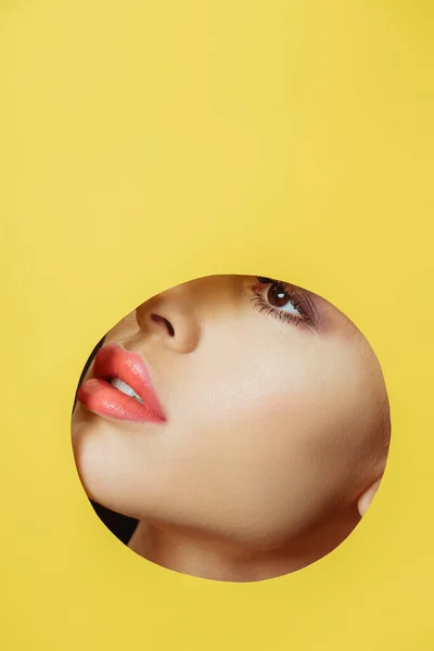 Female face with coral lips in round hole in yellow paper — Stock Photo