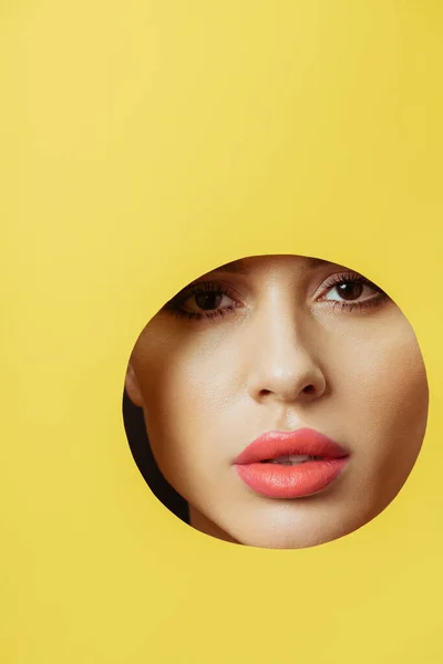 Mulher com lábios de coral olhando para a câmera através do buraco redondo em papel amarelo — Fotografia de Stock