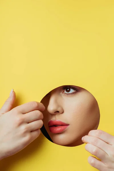 Donna con labbra di corallo guardando attraverso foro rotondo e toccando carta gialla con le mani — Foto stock