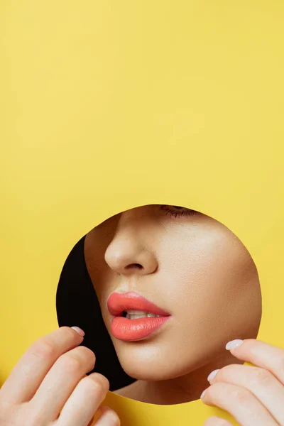 Cropped view of woman with coral lips touching yellow paper with hands on black — Stock Photo