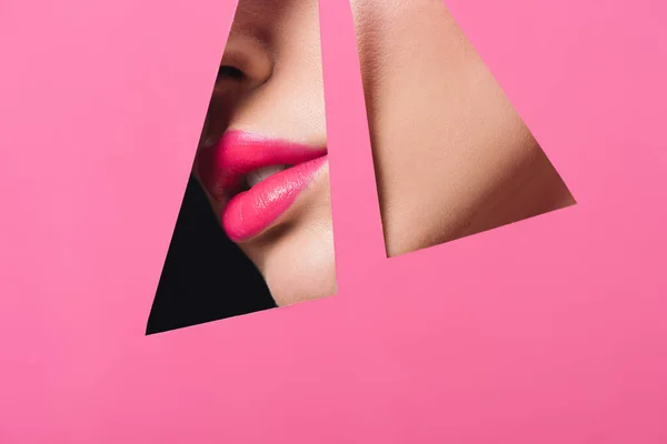 Cropped view of female face with pink lips across triangular holes in paper on black — Stock Photo