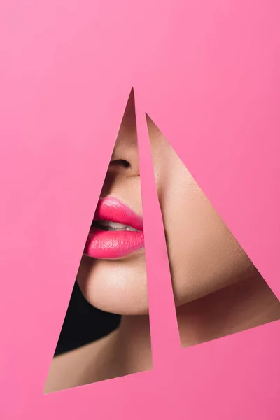 Vista recortada de la cara femenina con labios rosados en agujeros triangulares en papel sobre negro - foto de stock