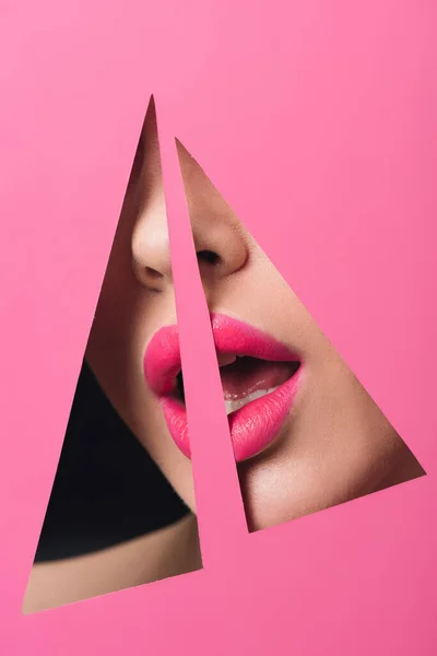 Vista recortada de mujer con labios rosados y boca abierta en agujeros triangulares en papel sobre negro - foto de stock