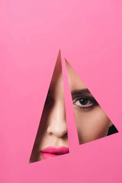 Девушка с дымчатыми глазами и розовыми губами, смотрящая на камеру через треугольные отверстия в бумаге — стоковое фото