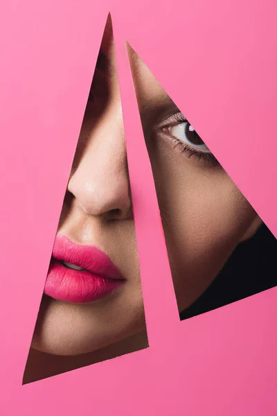 Chica con labios rosados mirando a la cámara a través de agujeros triangulares en papel sobre fondo negro - foto de stock