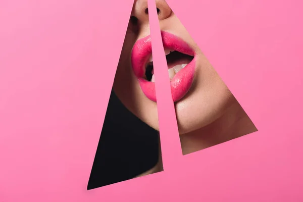 Vista recortada de mujer con labios rosados y boca abierta a través de agujeros triangulares en papel sobre negro - foto de stock