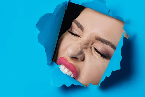 Woman with closed eyes and pink lips biting ripped blue paper on black — Stock Photo