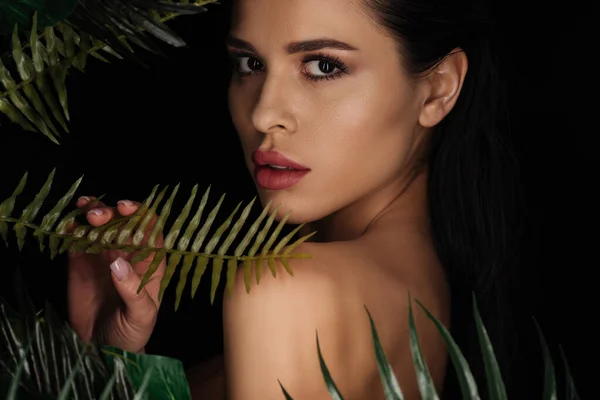 Beautiful woman touching fern leaf and looking at camera isolated on black — Stock Photo