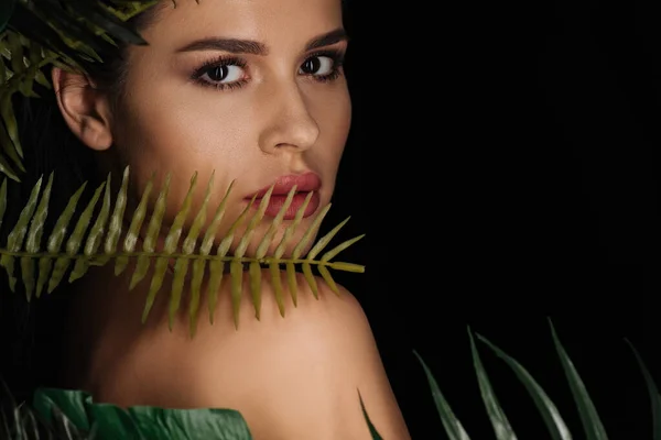 Retrato de mujer hermosa con hojas verdes mirando a la cámara aislada en negro - foto de stock