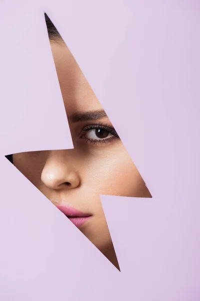 Girl looking at camera across hole in violet paper — Stock Photo