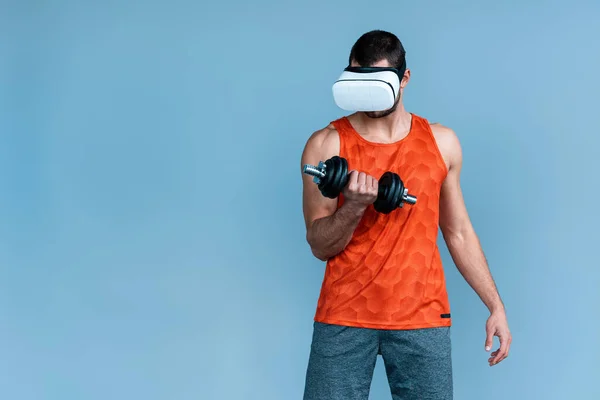 Sportsman in virtual reality headset working out with dumbbell isolated on blue — Stock Photo