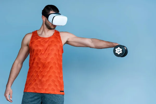 Hombre en auriculares de realidad virtual trabajando con mancuerna en azul - foto de stock