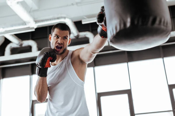 Foco seletivo do homem com raiva em luvas de boxe exercendo com saco de perfuração — Fotografia de Stock