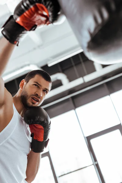 Selective focus of sportsman in boxing gloves exercising with punching bag — Stock Photo