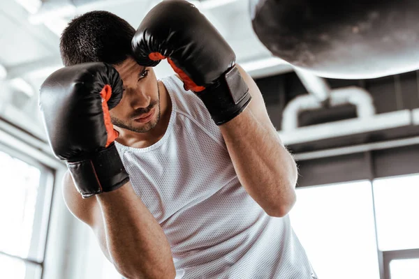 Enfoque selectivo del deportista en el entrenamiento de guantes de boxeo con saco de boxeo - foto de stock