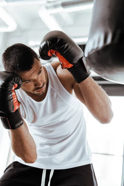 Enfoque selectivo del hombre guapo en el entrenamiento de guantes de boxeo con saco de boxeo - foto de stock