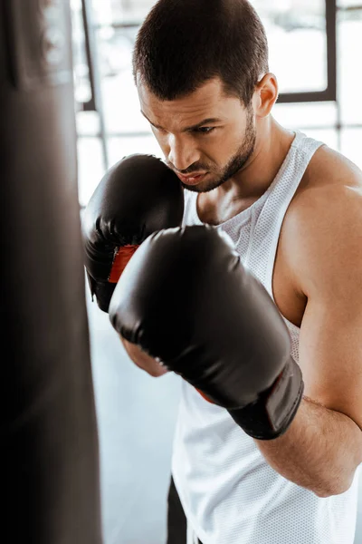 Foco seletivo do homem atlético no treinamento de luvas de boxe com saco de perfuração — Fotografia de Stock