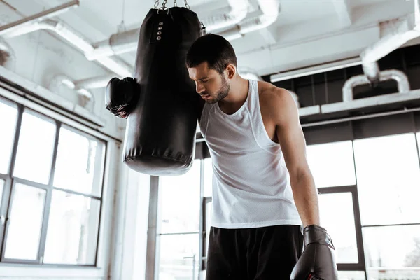 Уставший спортсмен в боксерских перчатках стоит рядом с боксерской грушей — стоковое фото