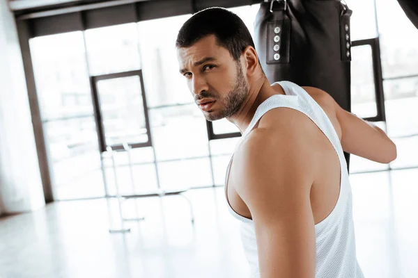 Enfoque selectivo de deportista guapo mirando la cámara cerca del saco de boxeo - foto de stock