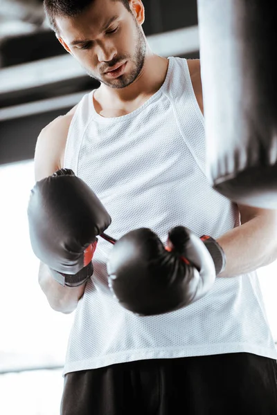 Избирательный фокус спортсмена, смотрящего на черные боксерские перчатки в спорткомплексе — стоковое фото