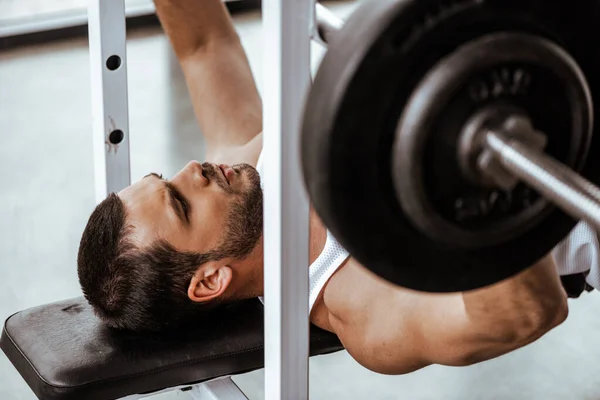 Foco seletivo de homem bonito exercitando com barbell no ginásio — Fotografia de Stock