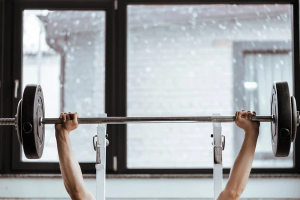Cropped view of strong sportsman working out with barbell in gym — Stock Photo