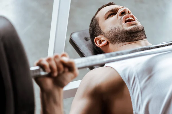 Selective focus of emotional sportsman working out with barbell in gym — Stock Photo