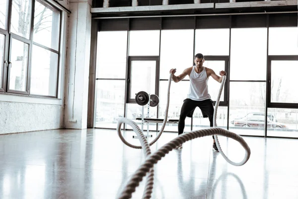 Foco seletivo do desportista exercitando com cordas de batalha no ginásio moderno — Fotografia de Stock