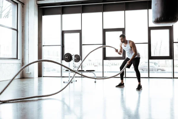 Foco seletivo de forte desportista exercitando com cordas de batalha no ginásio moderno — Fotografia de Stock