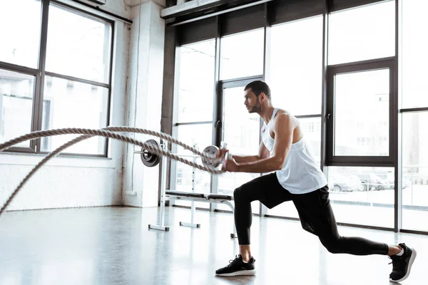 Deportista barbudo haciendo ejercicio con cuerdas de batalla en el gimnasio moderno — Stock Photo