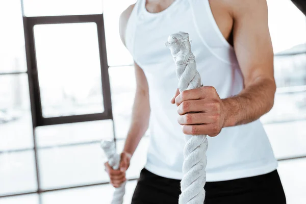 Vue recadrée d'un sportif faisant de l'exercice avec des cordes de combat dans une salle de gym — Photo de stock