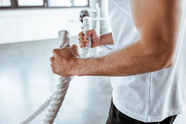 Vista cortada de desportista forte exercício com cordas de batalha no ginásio — Fotografia de Stock