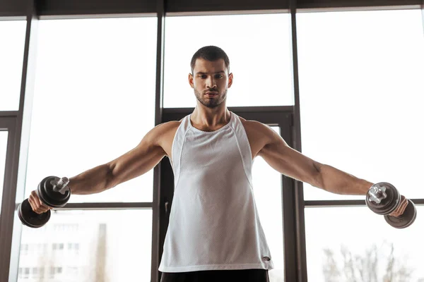 Athletic man with outstretched hands exercising with dumbbells in gym — Stock Photo