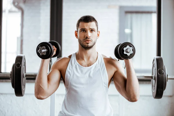 Athletic sportsman holding dumbbells while working out in gym — Stock Photo