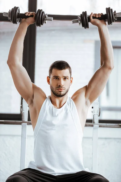 Strong sportsman holding dumbbells above head while exercising in gym — Stock Photo