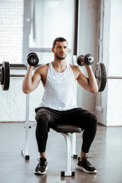 Athletic man holding dumbbells while working out near barbell in gym — Stock Photo