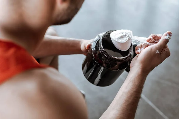 Vista recortada del deportista sosteniendo frasco y cuchara de medición con polvo de proteína - foto de stock