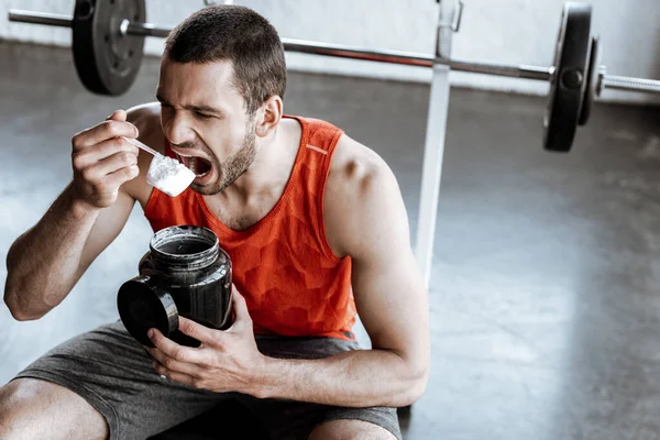 Sportif sportif avec bouche ouverte tenant pot et cuillère à mesurer avec de la poudre de protéines — Photo de stock