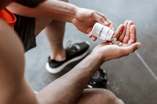 Vista recortada del deportista sosteniendo la botella con letras probióticas y pastillas en el gimnasio - foto de stock