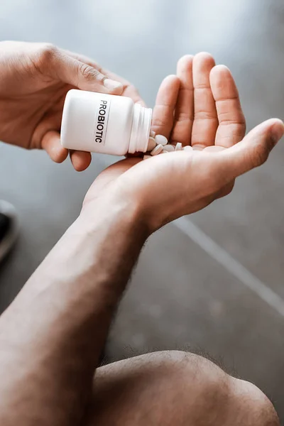 Cropped view of sportive man holding bottle with probiotic lettering and pills — Stock Photo