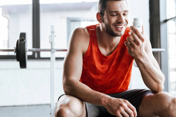 Happy sportsman looking at bottle with probiotic lettering in gym — Stock Photo