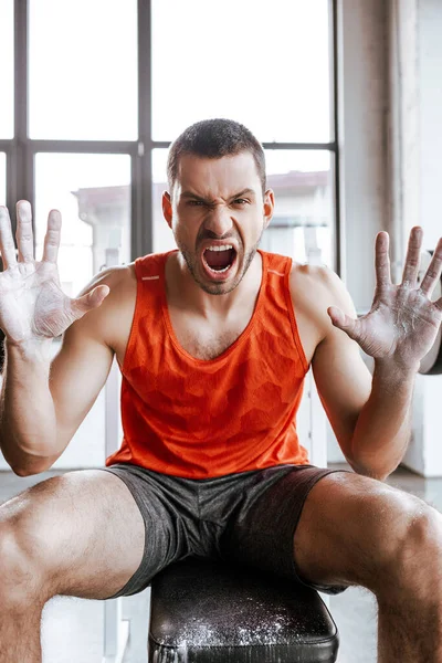 Emotional handsome sportsman with white powder on hands screaming in gym — Stock Photo